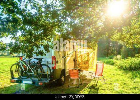 Ein camper mit Fahrrädern auf einem Heckträger steht in idylischer Umgebung im Sommer auf einer Wiese zwischen Bäumen, Vogesen, Frankreich. MIT einem Campervan unterwegs *** Un camper con biciclette su un portapacchi posteriore si erge in un ambiente idilliaco in estate su un prato tra alberi, Vosgi, Francia che viaggia con un camper Foto Stock