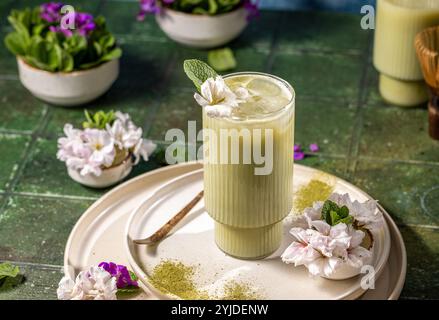 Rinfrescante latte matcha freddo decorato con menta fresca e delicati fiori di ciliegio, servito su un elegante piatto con polvere di matcha Foto Stock