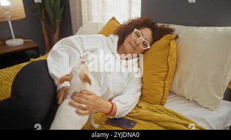 Una donna anziana in una camera da letto giace su un letto con chihuahua, mostrando relax e compagnia in un accogliente ambiente interno. Foto Stock