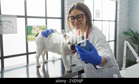 Giovane, bionda, caucasica, donna veterinaria in una clinica fa un selfie con un piccolo, bianco, cane animale domestico in una stanza d'ospedale. Foto Stock