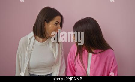 Due donne, vestite in modo informale, impegnate in una conversazione con sfondo rosa, probabilmente amici o sorelle intimi. Foto Stock