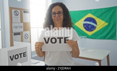 Donna con un segno di voto in una sala di voto con bandiera brasiliana. Foto Stock