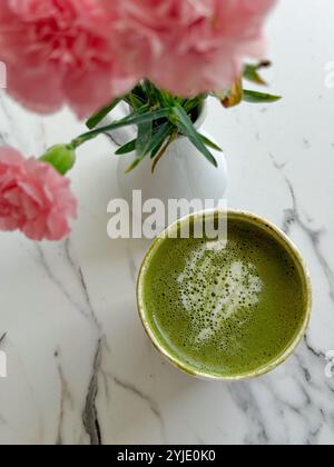 Una bella tazza di tè matcha con fiori rosa freschi su un tavolo di marmo Foto Stock