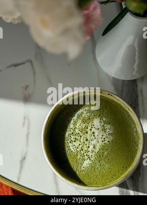 Una bella tazza di tè matcha con fiori rosa freschi su un tavolo di marmo Foto Stock