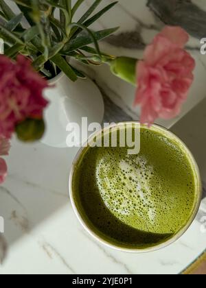 Una bella tazza di tè matcha con fiori rosa freschi su un tavolo di marmo Foto Stock