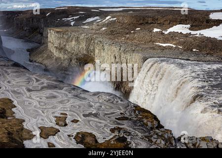 Arcobaleno sopra la cascata Dettifoss nel Parco Nazionale Vatnajokull nel nord-est dell'Islanda, vista delle cascate e del canyon con colonne basaltiche, ghiaccio e neve. Foto Stock