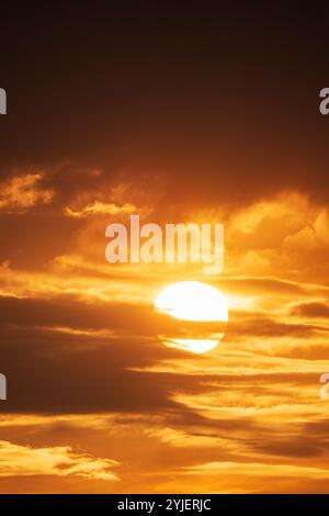 Una vista spettacolare del sole che tramonta dietro strati di nuvole, proiettando una calda luce dorata sul cielo Foto Stock