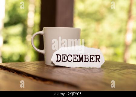 Ciao testo di dicembre scrivi su un cartoncino di carta con cavalletto in legno e decorazioni floreali su sfondo in legno Foto Stock