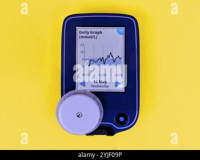 Dispositivo per il monitoraggio continuo del glucosio – CGM e sensore bianco. Grafico giornaliero sullo schermo. Sfondo giallo. Diabete di tipo 1. L'insulina dipende Foto Stock