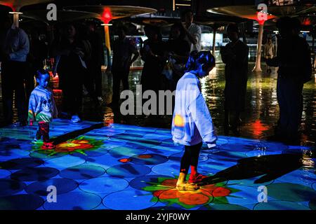 Bangkok, Thailandia. 14 novembre 2024. I bambini hanno camminato sul sentiero con le luci illuminate del Krathong virtuale a terra durante il festival Loy Krathong a Bangkok. Il Virtual Loy Krathong con tecnologia di mappatura della proiezione ha avuto luogo presso il passerella Pathum Wan di Bangkok, con l'obiettivo di ridurre gli sprechi nell'annuale festival Loy Krathong. (Immagine di credito: © Wissarut Weerasopon/ZUMA Press Wire) SOLO PER USO EDITORIALE! Non per USO commerciale!/Alamy Live News Foto Stock