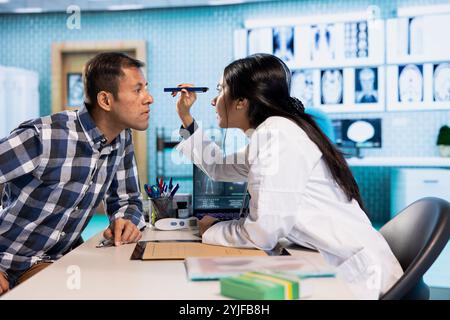 Optometrista che esegue un test di visione in un moderno ufficio clinico. Paziente indiano sottoposto a un esame oculistico, ottico che utilizza strumenti diagnostici per la correzione della vista e il trattamento in una consultazione. Foto Stock