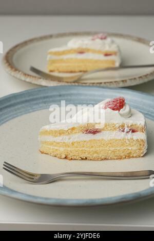 Shortcake e forchetta di fragole giapponesi su ogni piatto grande e piccolo su un tavolo bianco. Foto Stock
