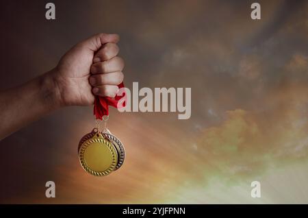 Uomo che tiene in mano medaglie d'oro, d'argento e di bronzo contro il cielo del tramonto, primo piano Foto Stock