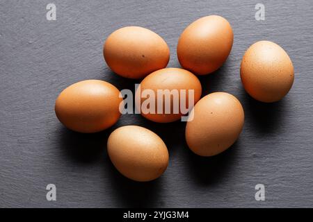 Sette uova marroni giacciono sparse su una superficie di ardesia grigia. Le uova sono disposte in modo casuale, con qualche sovrapposizione. L'immagine viene acquisita da un sl Foto Stock