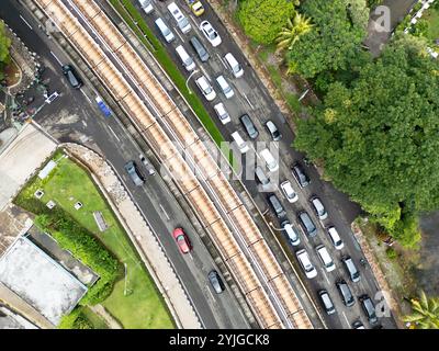 Vista dall'alto di una strada trafficata a Giacarta con un binario ferroviario sopraelevato che corre lungo, trasporto urbano e infrastrutture, vita cittadina in Indonesia Foto Stock