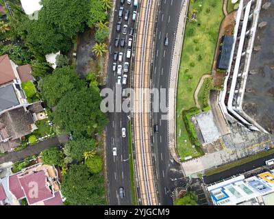 Vista dall'alto di una strada trafficata a Giacarta con un binario ferroviario sopraelevato che corre lungo, trasporto urbano e infrastrutture, vita cittadina in Indonesia Foto Stock