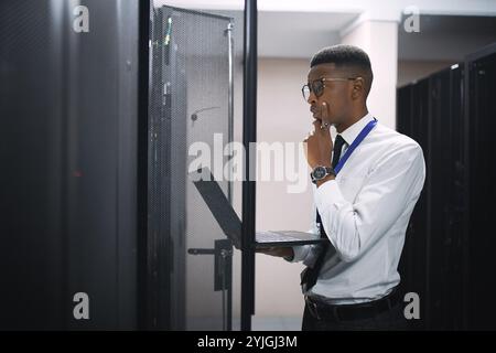 Uomo nero, ingegnere e risoluzione dei problemi con notebook in sala server per la riparazione di software, hardware o rete. Uomo, tecnico IT o pensiero Foto Stock