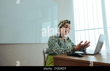 Donna d'affari indiana si impegna con passione in una riunione d'affari virtuale da un ufficio contemporaneo. I suoi gesti espressivi evidenziano un efficace commun Foto Stock