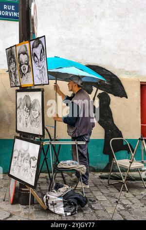 Montmartre, Parigi, 22 luglio 2024: Un artista di strada che regge un ombrello mentre un disegno di una coppia con ombrello è sul muro accanto a lui. Foto Stock