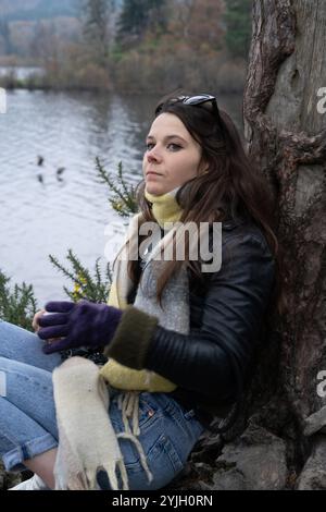 Giovane donna che si rilassa sul lago con tè nel paesaggio autunnale del Lake District Foto Stock