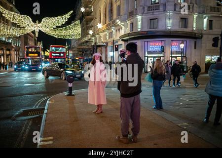 Una donna che fa scattare la sua foto mentre si trova al Piccadilly Circus con decorazioni natalizie appese illuminate sull'Haymarket alle sue spalle nel West End di Londra Foto Stock