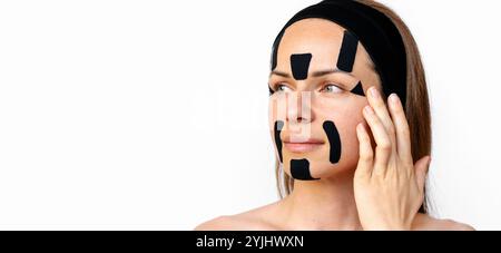 Ritratto di bellezza di una donna caucasica che applica nastri di kinesiologia nera sul viso. Foto Stock