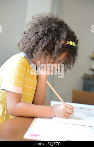 Bambino in abito giallo focalizzato sulla scrittura con una matita su un tabl Foto Stock