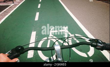 Vista in prima persona del manubrio mentre si pedala su una pista ciclabile verde designata, promuovendo un trasporto urbano sostenibile Foto Stock