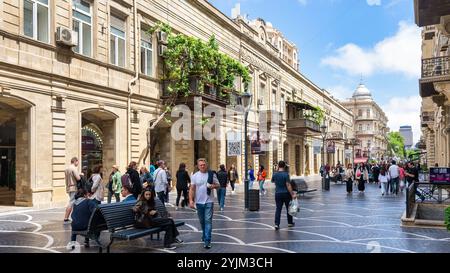 Baku, Azerbaigian - 5 maggio 2024: Via Nizami è piena di attività mentre i pedoni passeggiano sotto un cielo azzurro. Lussureggiante vegetazione adorna i balconi, esaltando l'atmosfera vibrante Foto Stock