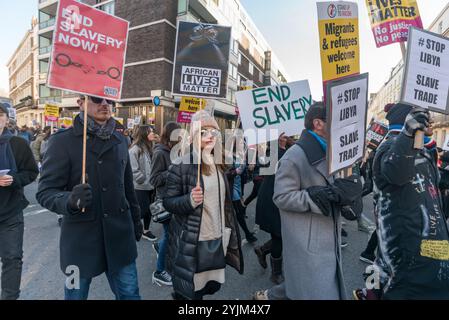 Londra, Regno Unito. 9 dicembre 2017. Un uomo in abiti bianchi conclude una cerimonia di libagione africana in onore degli eroi delle lotte africane gettando acqua sulla folla alla protesta di fronte all'ambasciata libica contro la vendita di neri africani da parte di commercianti arabi di schiavi in Libia. La marcia ospitata da African Lives Matter ha richiesto la chiusura dei centri di detenzione libici, l'azione dei governi africani per salvare le persone detenute nei campi e la condanna del commercio di schiavi e degli omicidi di migranti da parte di tutti i leader africani e delle Nazioni Unite, invitando la Libia a emanare e far rispettare leggi che impediscano queste crisi Foto Stock