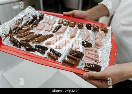 Cioccolatini assortiti su un vassoio con carta nelle mani di un pasticcere. Foto di alta qualità Foto Stock