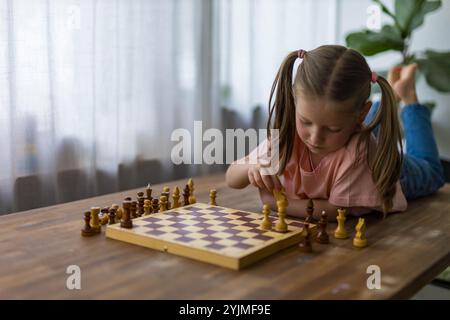 la bambina di 5 anni gioca a miniscacchi, pianificando attentamente la sua prossima mossa in un momento di apprendimento divertente. Foto di alta qualità Foto Stock