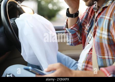 Uomo che usa lo smartphone vicino all'airbag aperto in auto dopo un incidente d'auto, primo piano Foto Stock