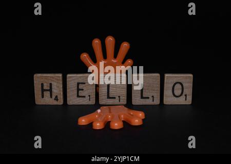 Due mani di giocattolo arancioni che tengono in mano le lettere dello scraper formano la parola "CIAO" Foto Stock