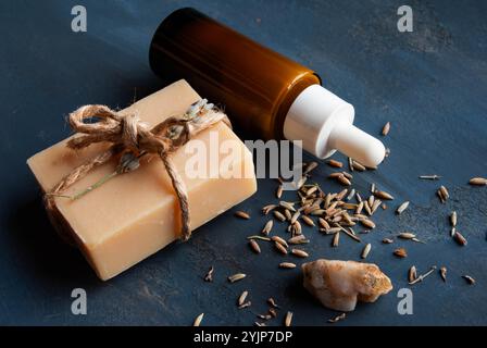 Sapone lavanda fatto a mano avvolto da un fiocco rustico, abbinato a un siero lavanda, splendidamente visualizzato su uno sfondo blu scuro. Foto Stock