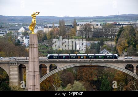 Lussemburgo, Lussemburgo. 15 novembre 2024. Un tram attraversa il ponte Adolphe a Lussemburgo. In primo piano si trova la "Gëlle FRa'" (donna d'oro), un cosiddetto memoriale di guerra con una statua in bronzo dorato di una donna su un obelisco di granito. Credito: Harald Tittel/dpa/Alamy Live News Foto Stock