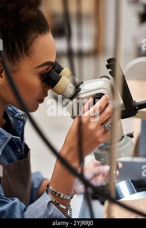 Una donna di talento si concentra intensamente sull'esame di gioielli scintillanti utilizzando un microscopio nel suo studio. Foto Stock