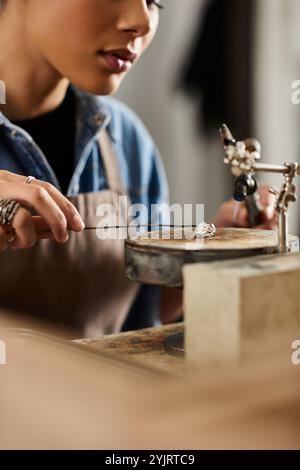 Un'artigiana modella delicatamente un bellissimo gioiello mentre si concentra nel suo invitante laboratorio Foto Stock