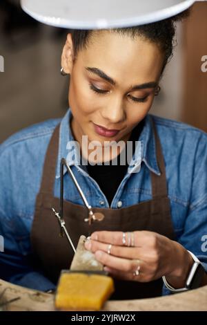 La talentuosa artigiana si concentra intensamente sulla sua creazione di gioielli con precisione e passione. Foto Stock