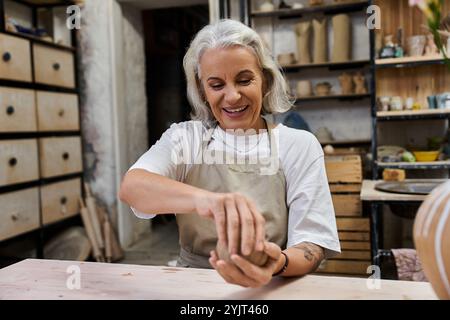 Una bella donna matura modella con gioia l'argilla mentre è immersa nel suo laboratorio di ceramiche creative. Foto Stock