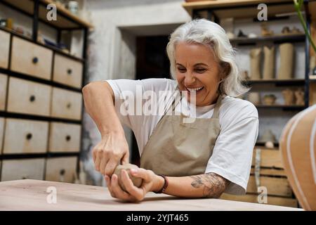 Una donna allegra e matura sta modellando l'argilla con attenzione e passione nel suo spazio artistico Foto Stock