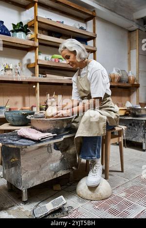 Un artigiano di talento si concentra intensamente sullo stampaggio dell'argilla, avvolto in uno spazio di lavoro caldo e stimolante. Foto Stock