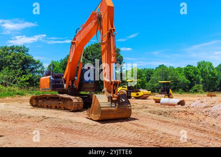 Un escavatore sta scavando nella terra mentre due rulli stanno preparando il terreno nell'area del cantiere è lussureggiante Foto Stock