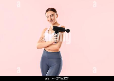 Giovane donna con massaggiatore percussivo su sfondo rosa Foto Stock