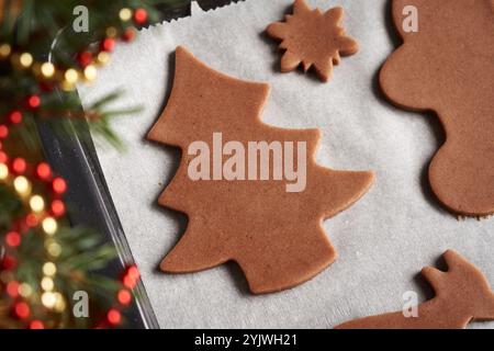 Albero e altre forme tagliate dall'impasto crudo su un foglio di carta da forno, preparando biscotti di Natale fatti in casa di pan di zenzero Foto Stock