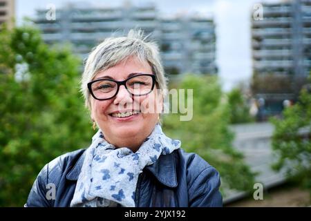 Ritratto di gioiosi occhiali da donna senior grigi in posa felici con giardino urbano di sfondo non focalizzato. Foto Stock