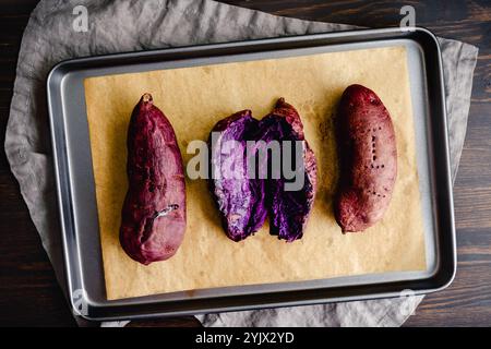 Patate dolci viola arrosto su una teglia: Patate dolci viola cotte intere e affettate su una teglia rivestita di carta pergamena Foto Stock