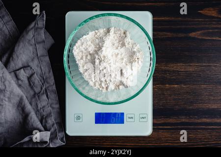 Pesatura della farina multiuso su una bilancia digitale da cucina: Vista dall'alto della farina di frumento sbiancata in un recipiente di vetro pesato su una bilancia alimentare Foto Stock