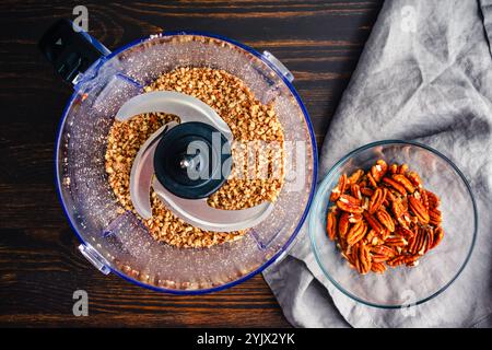 Macinare le noci pecan in una ciotola del robot da cucina: Vista dall'alto delle noci pecan finemente macinate in un robot da cucina su un tavolo di legno Foto Stock