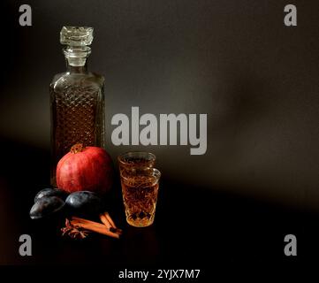 Liquore di prugne melograno con cannella e anice su sfondo nero, forte alcol fatto in casa con spezie e in vetro di cristallo. Primo piano. Foto Stock